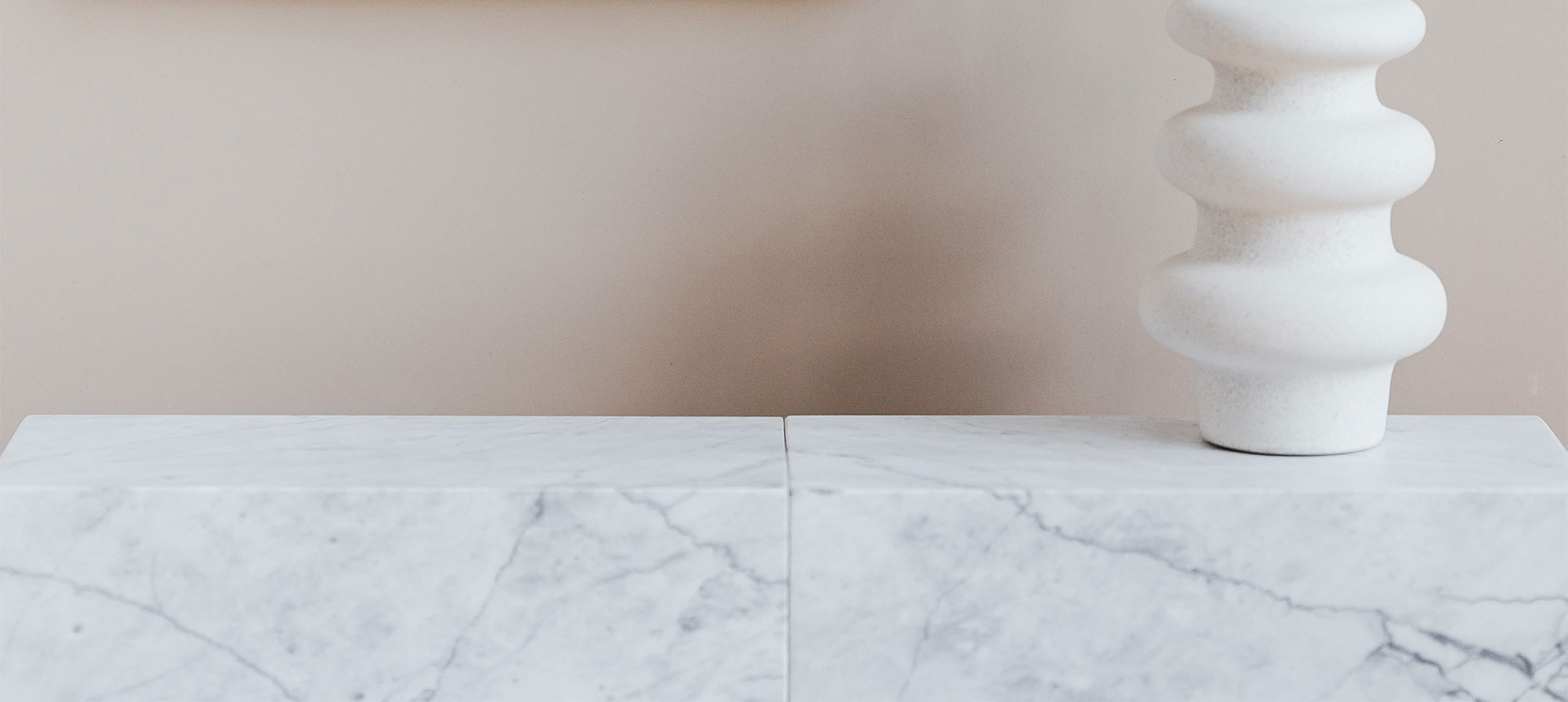 vit vas ståendes på marmorhylla med fallande skugga på rosa vägg